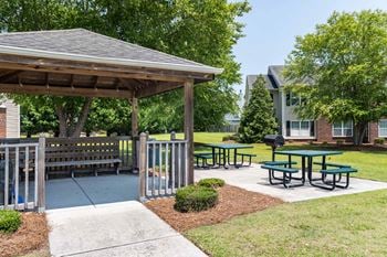 A pavilion with picnic tables is surrounded by a fence and a sidewalk.